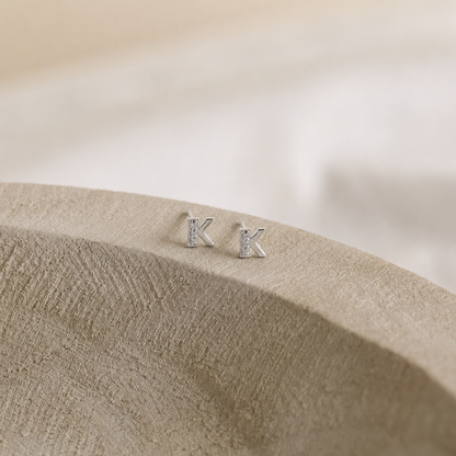 Silver 'K' earrings on a textured beige surface