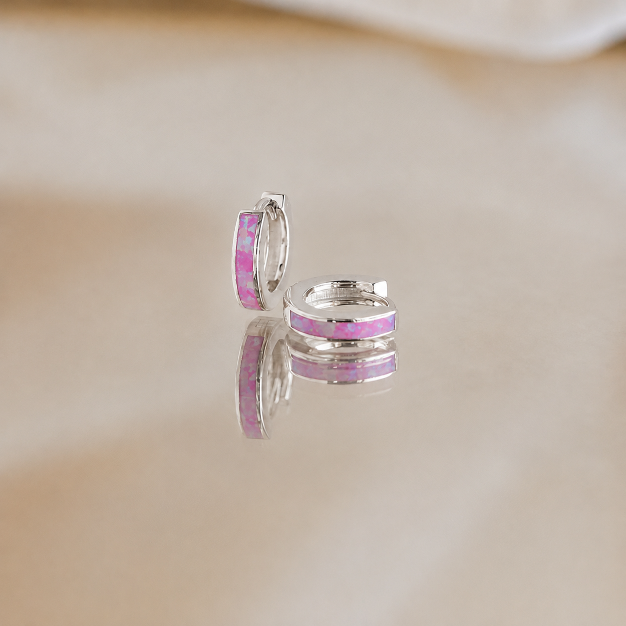Silver hoop earrings with pink gemstones on a beige background