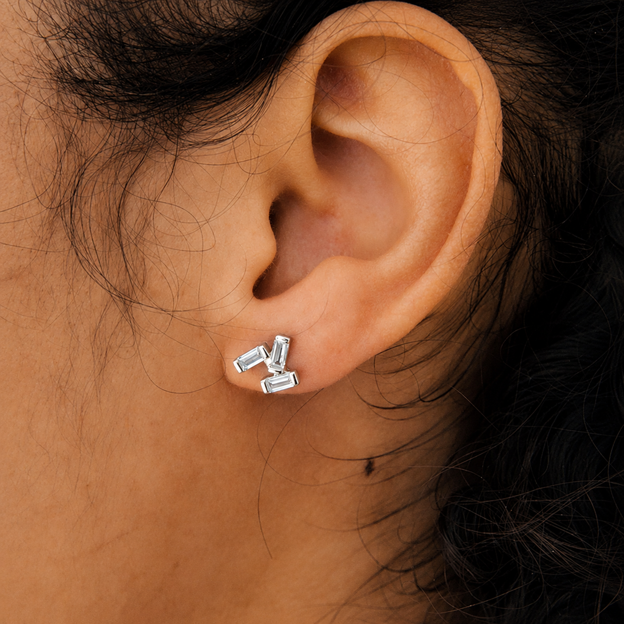 Close-up of an ear wearing silver rectangular stud earrings.
