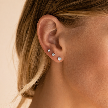 Close-up of an ear wearing diamond stud earrings on a beige background