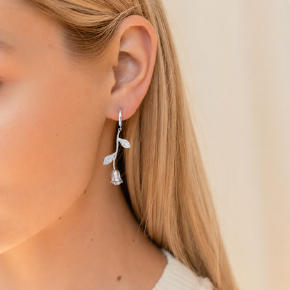 Silver floral earring worn by a person with a neutral background