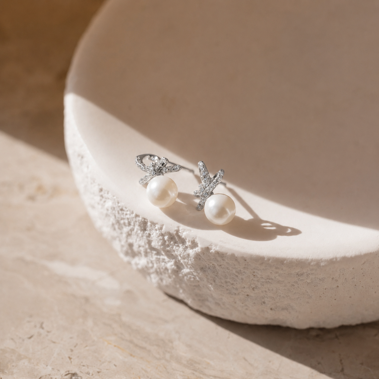 Pearl earrings with silver butterfly designs on a textured beige surface