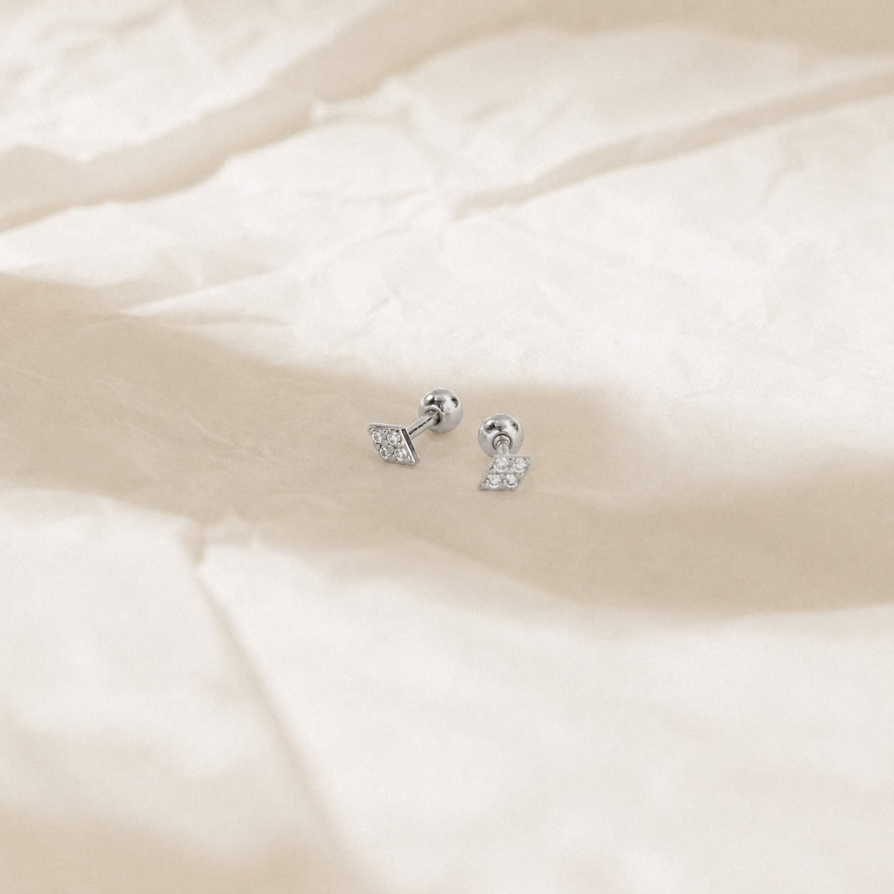 Pair of silver earrings on a soft beige fabric background