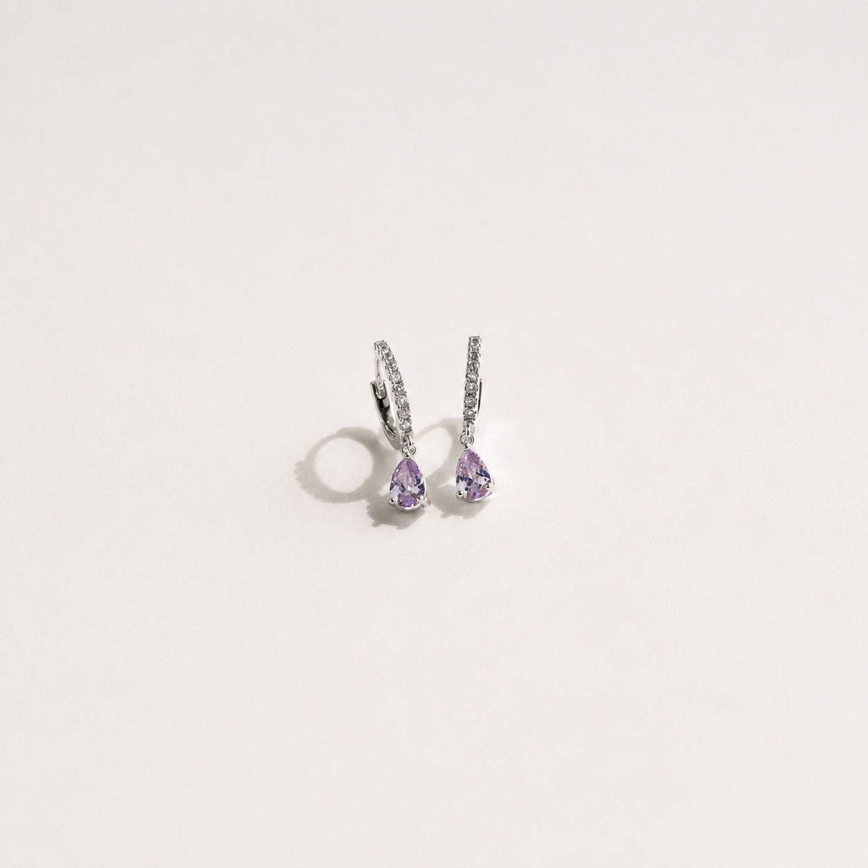 Pair of silver earrings with purple gemstones on a light gray background