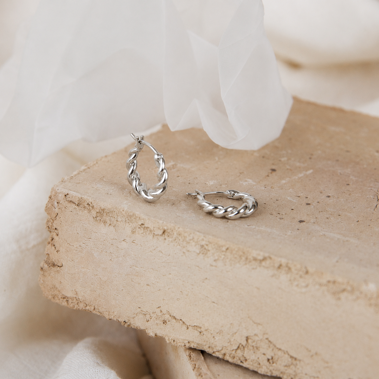 Silver hoop earrings on a textured stone surface with a soft white background