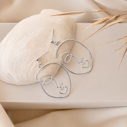 Silver heart-shaped earrings on a beige stone with natural elements