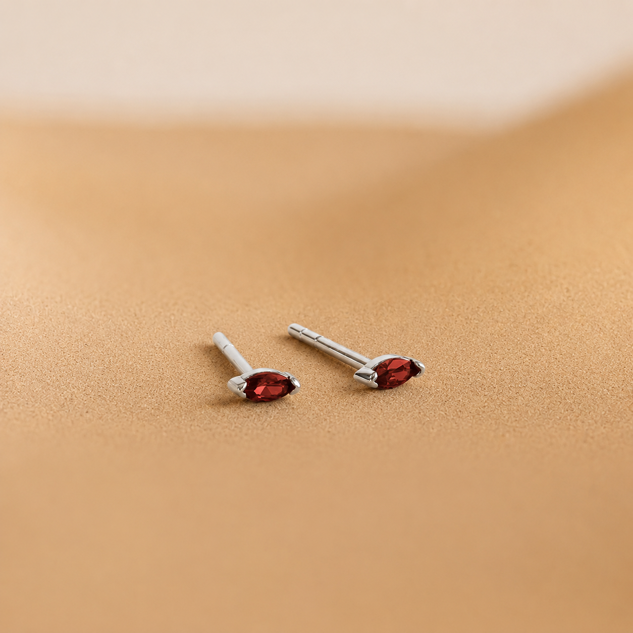 Pair of silver earrings with red gemstones on a beige background