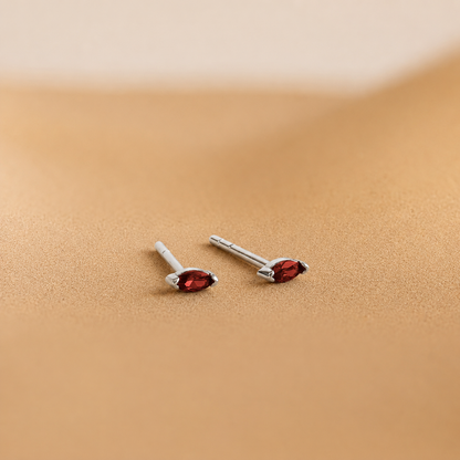 Pair of silver earrings with red gemstones on a beige background