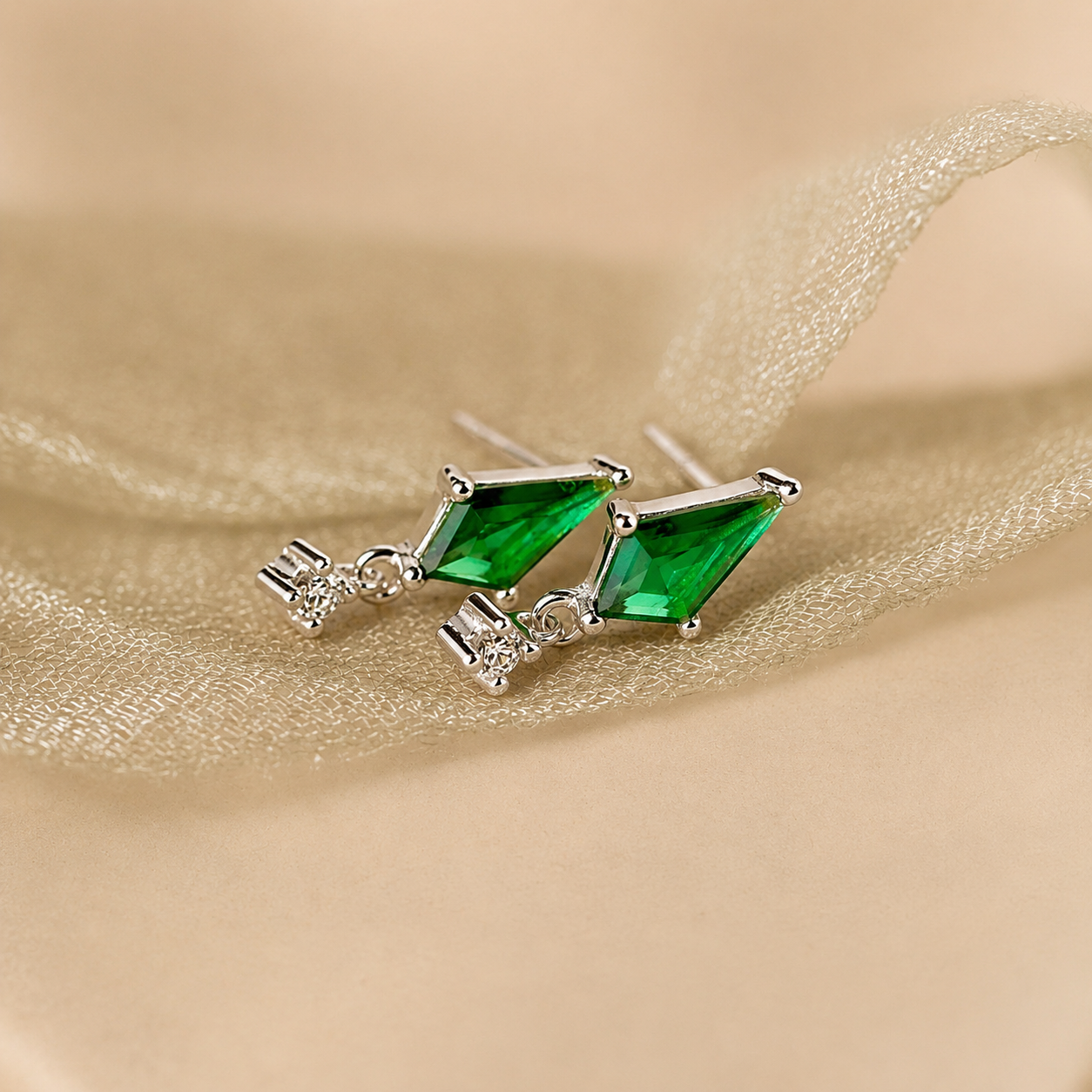 Pair of green gemstone earrings on a beige fabric background