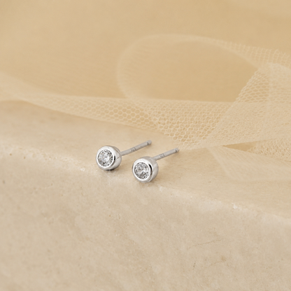 Pair of silver stud earrings with clear gemstones on a beige fabric background