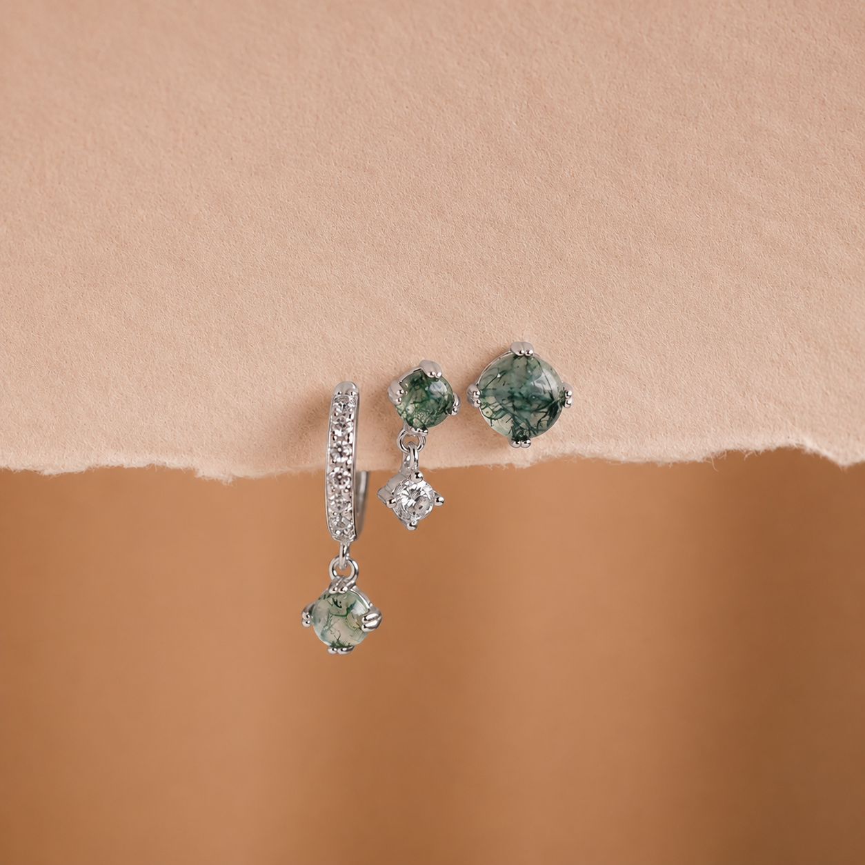 Pair of earrings with green gemstones on a beige background