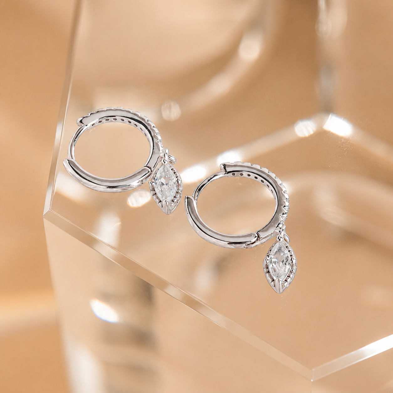 Silver hoop earrings with teardrop-shaped gemstones on a clear stand against a beige background