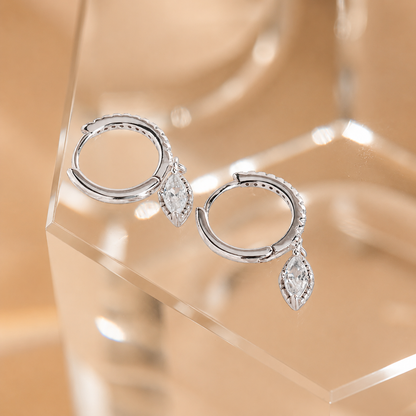 Silver hoop earrings with teardrop-shaped gemstones on a clear stand against a beige background